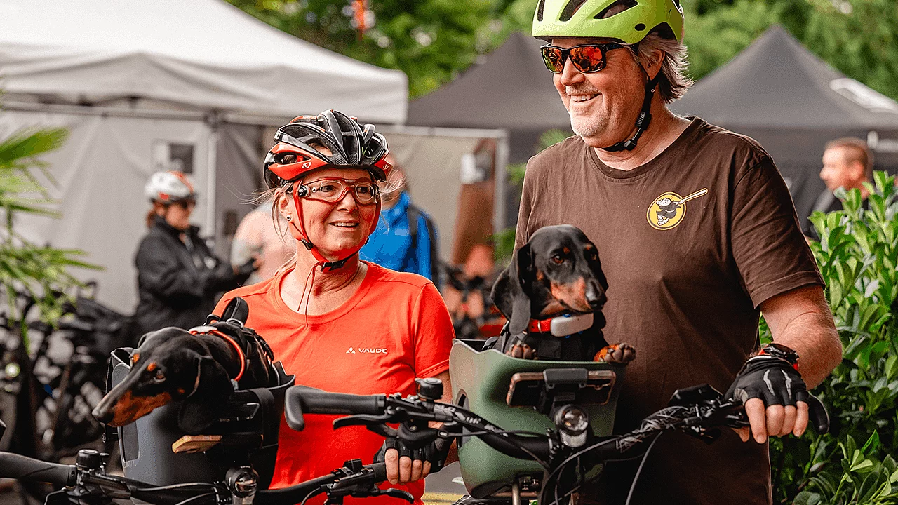 Teilnehmende einer Fahrradveranstaltung mit ihren Fahrrädern und zwei Dackeln in Transportkörben.