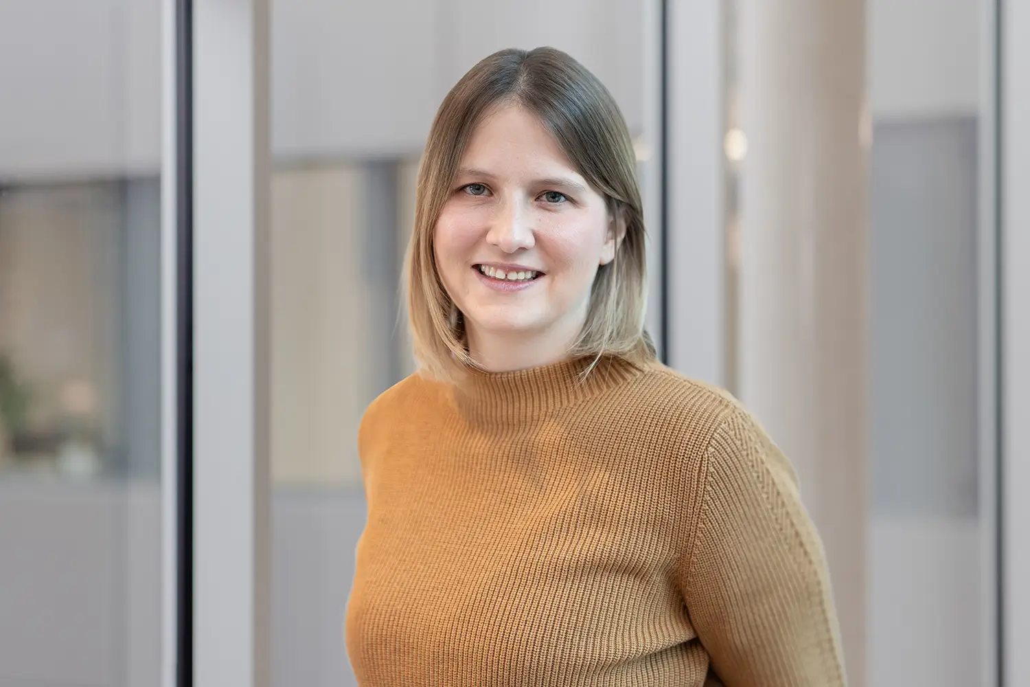 Porträt von Anna Kempf mit hellbraunem Rollkragenpullover vor einer Glasfront