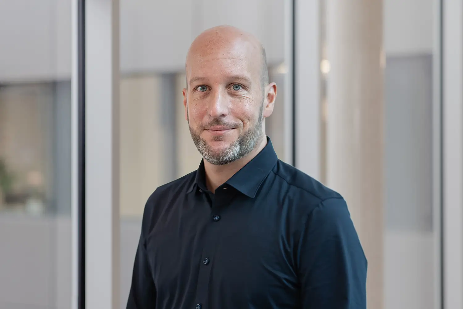 Porträt von Marius Müller mit dunklem Hemd vor einer Glasfront.