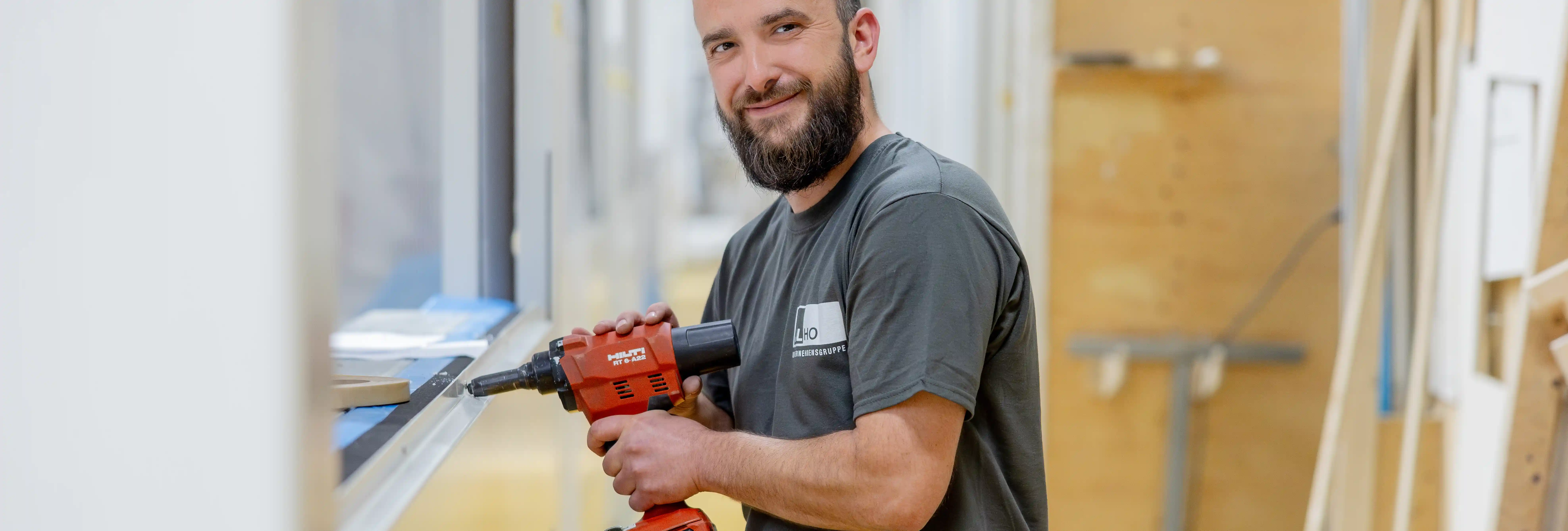 ALHO-Mitarbeiter mit Hilti-Bohrmaschine beim Innenausbau eines Modulgebäudes, lächelnd in die Kamera