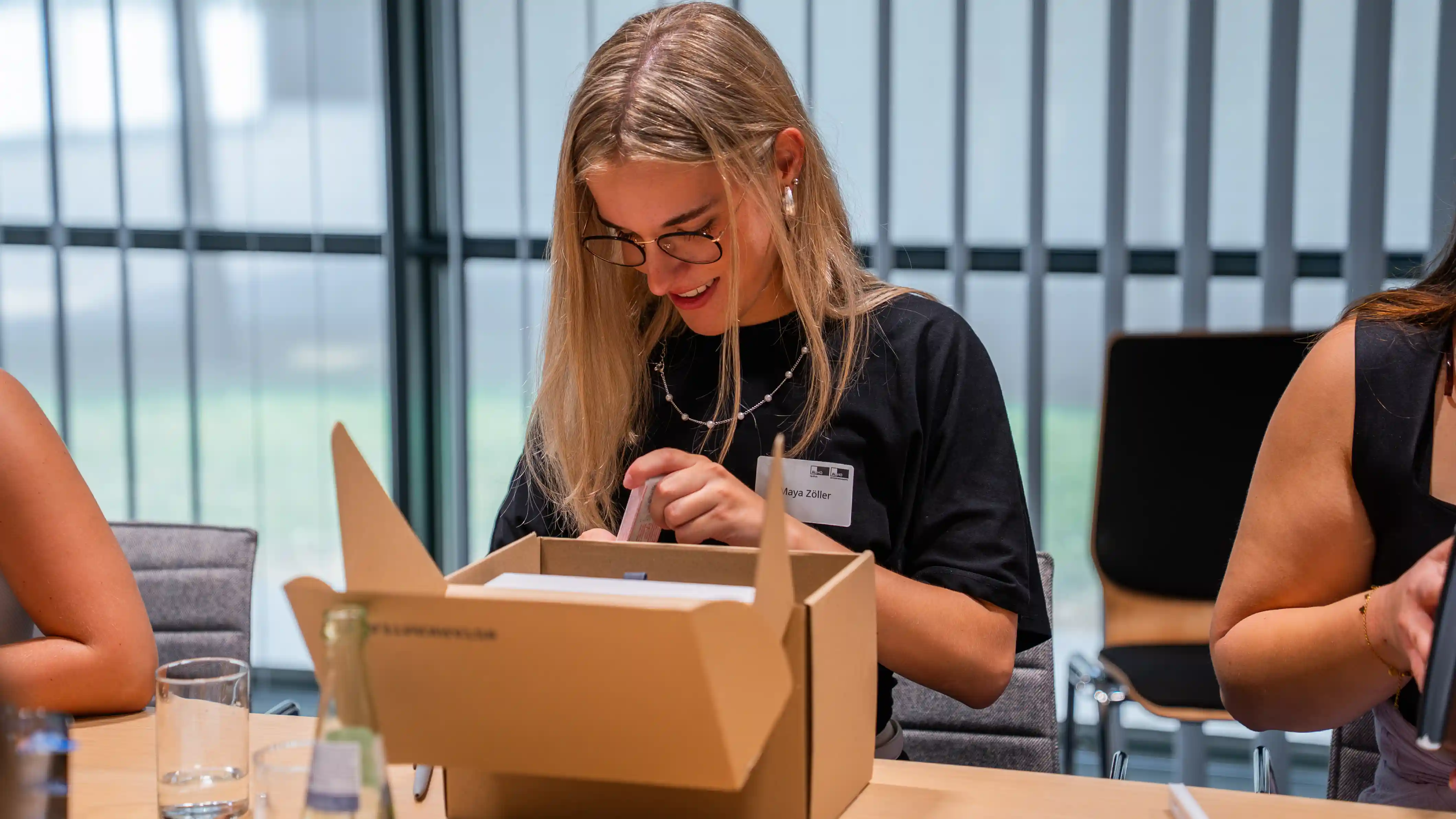 Auszubildende Maya Zöller packt am Tisch einen Willkommenskarton aus