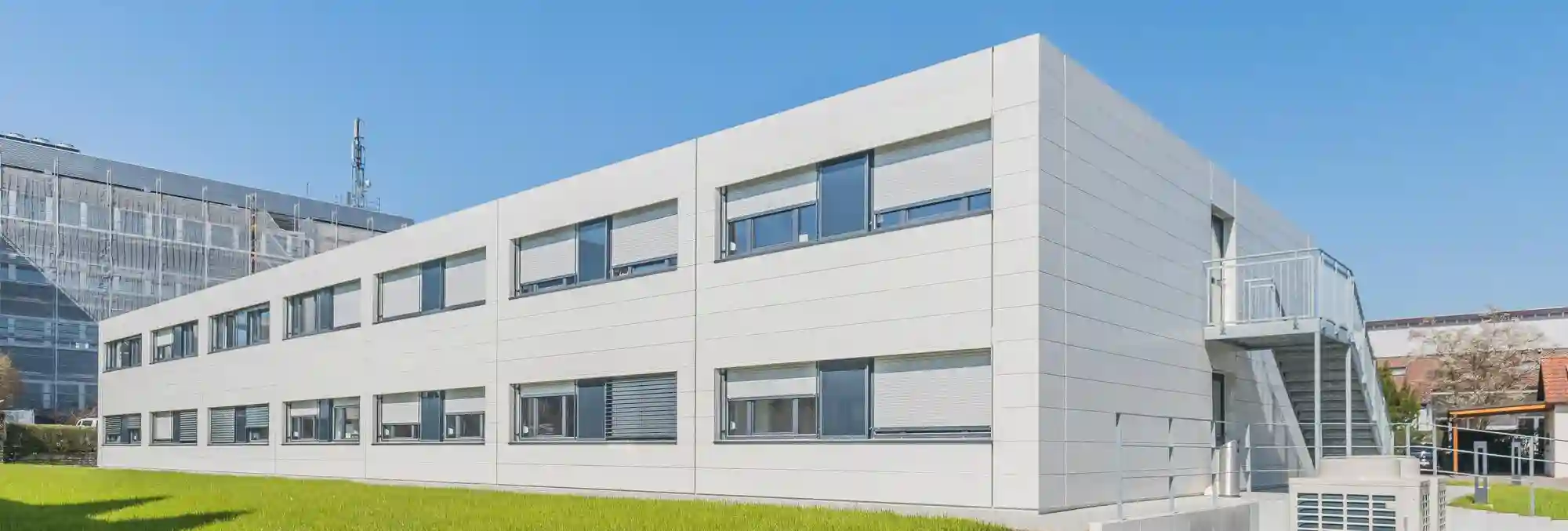 Bâtiment modulaire moderne à deux niveaux avec façade claire et larges fenêtres. La construction illustre une solution flexible et durable pour la gestion de capacités supplémentaires sur plusieurs sites.