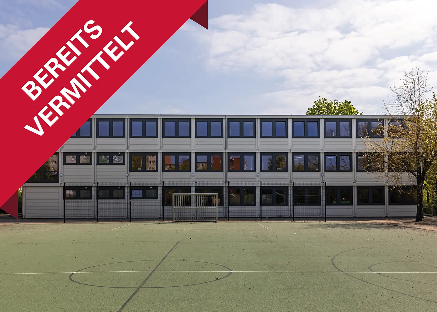 Modernes Schulgebäude mit Sporthof im Vordergrund – erfolgreich vermittelt.