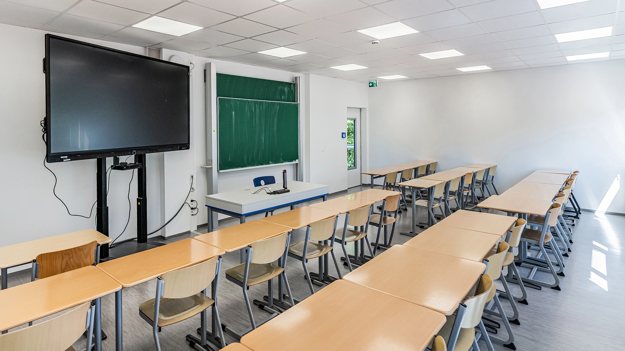 Klassenzimmer mit Tischen, Tafel, interaktivem Display und heller Deckenbeleuchtung