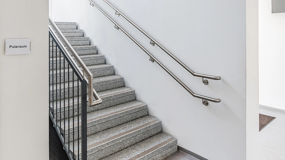 Treppenhaus mit grauer Steintreppe, Metallgeländer und Schild zum Putzraum