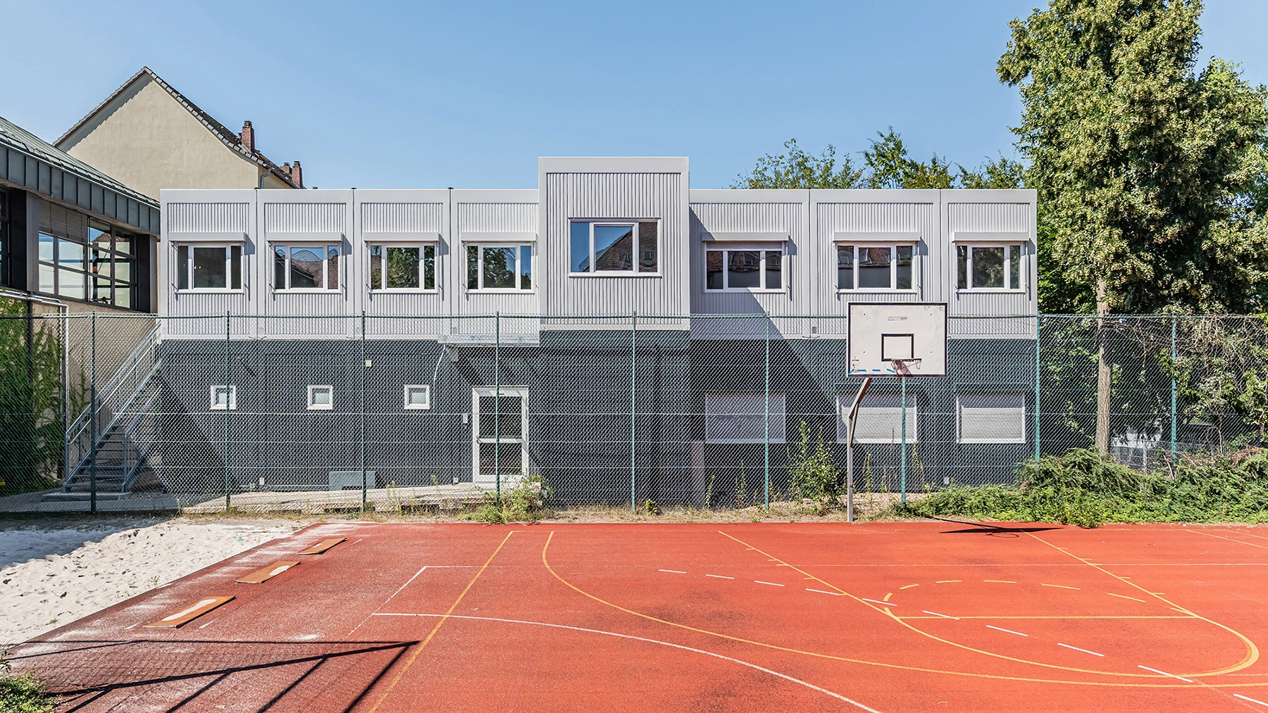 Schulgebäude in Containerbauweise hinter einem Sportplatz mit Basketballkorb