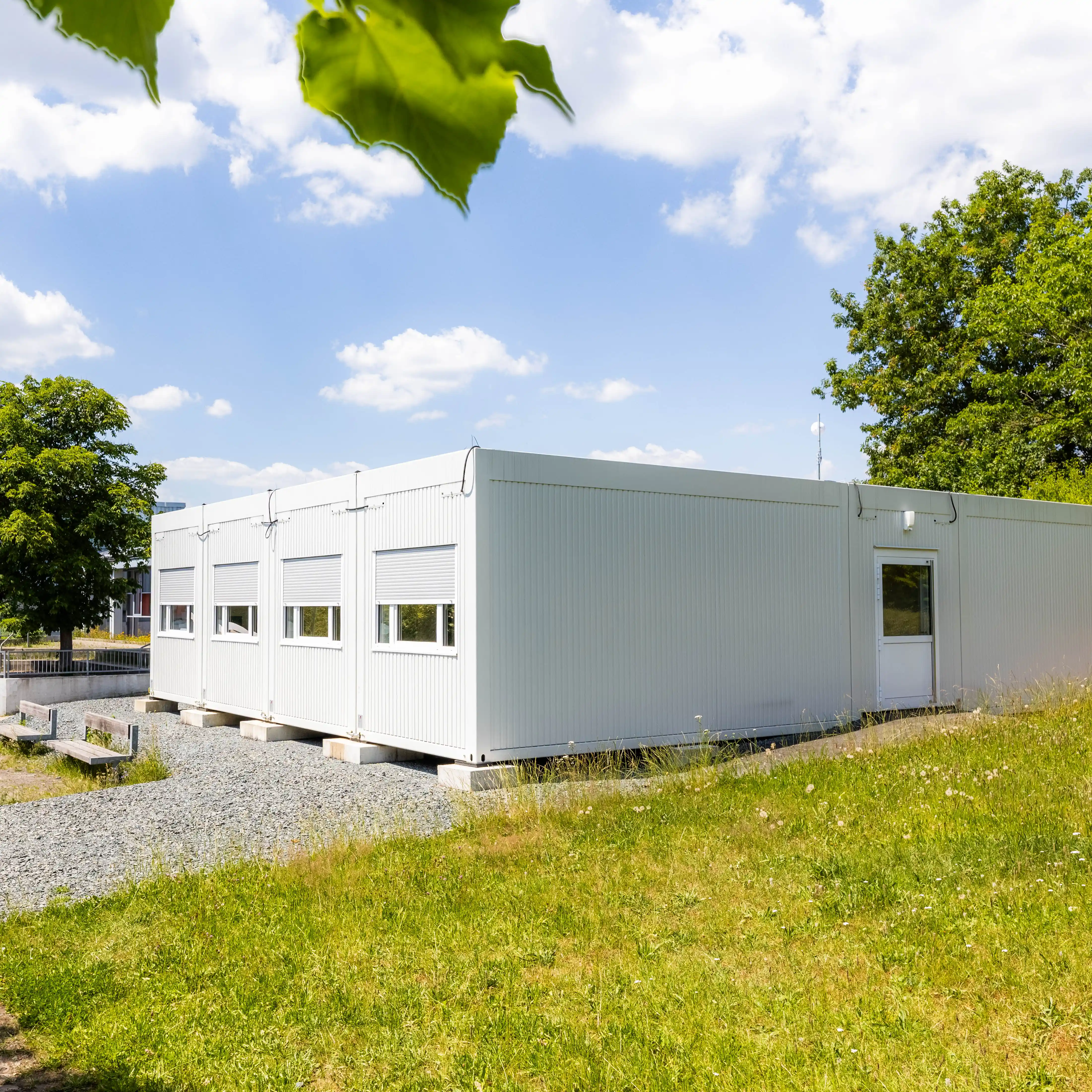 Temporäre Schulcontaineranlage mit mehreren Klassenräumen und Fensterreihen. Die ProENERGY-Anlage befindet sich auf dem Gelände der Pestalozzi-Schule und ist von Grünflächen und Bäumen umgeben.