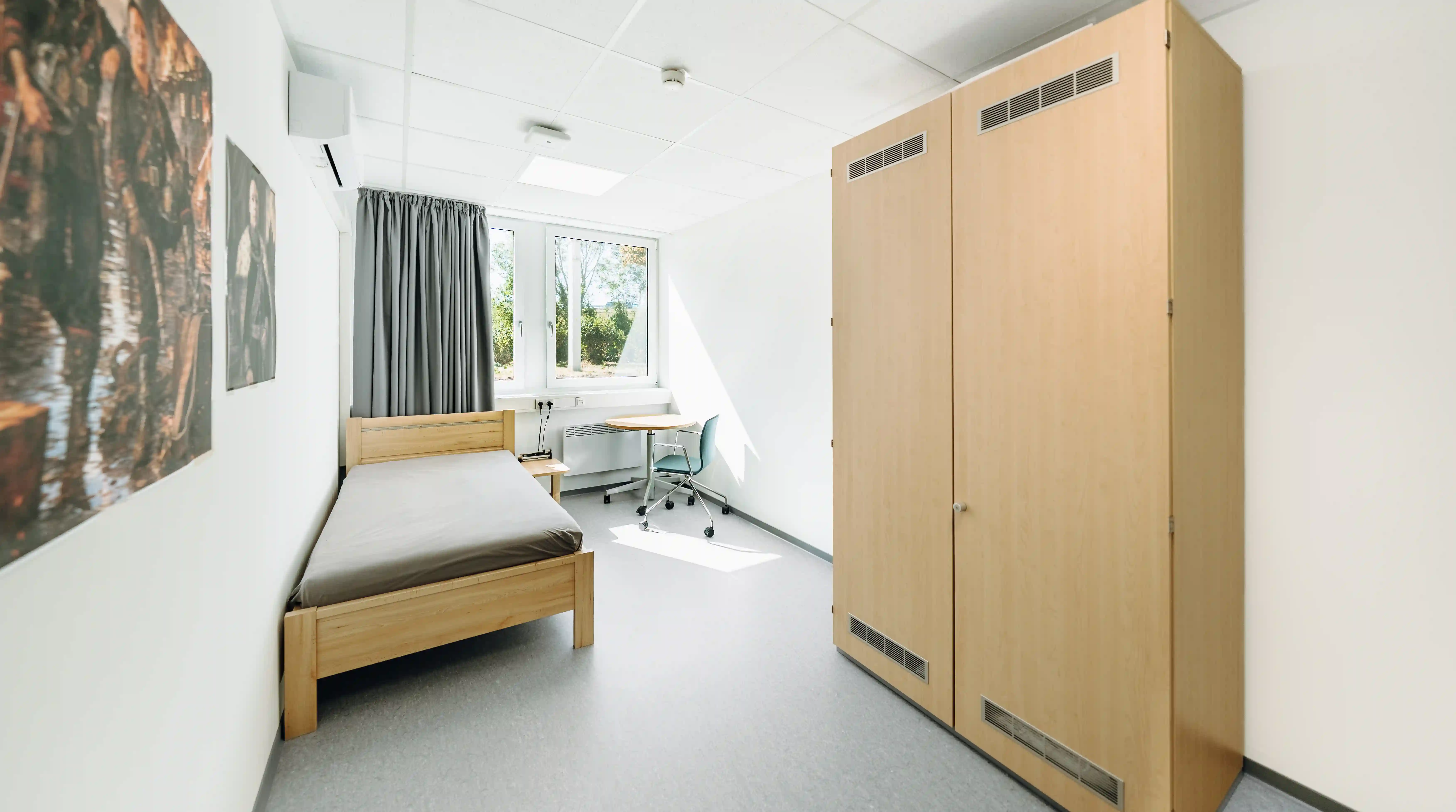 Modern eingerichtetes Einzelzimmer mit Bett, Kleiderschrank, Schreibtisch und Fenster. Der helle Raum bietet funktionale Unterbringungsmöglichkeiten für Beschäftigte oder Einsatzkräfte.