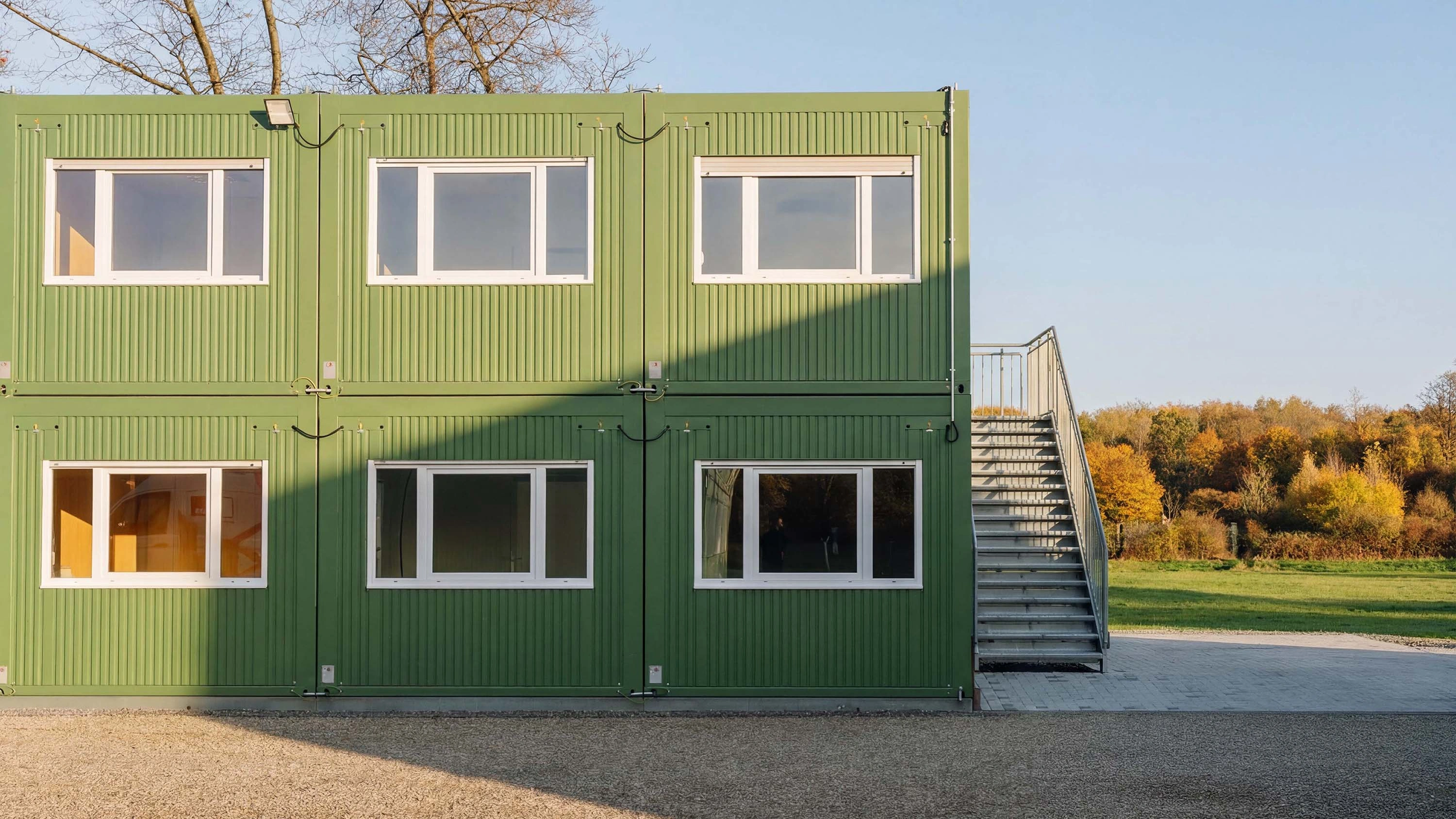 Zweigeschossige grüne Containeranlage mit Außentreppe, Fensterreihen und herbstlicher Umgebung
